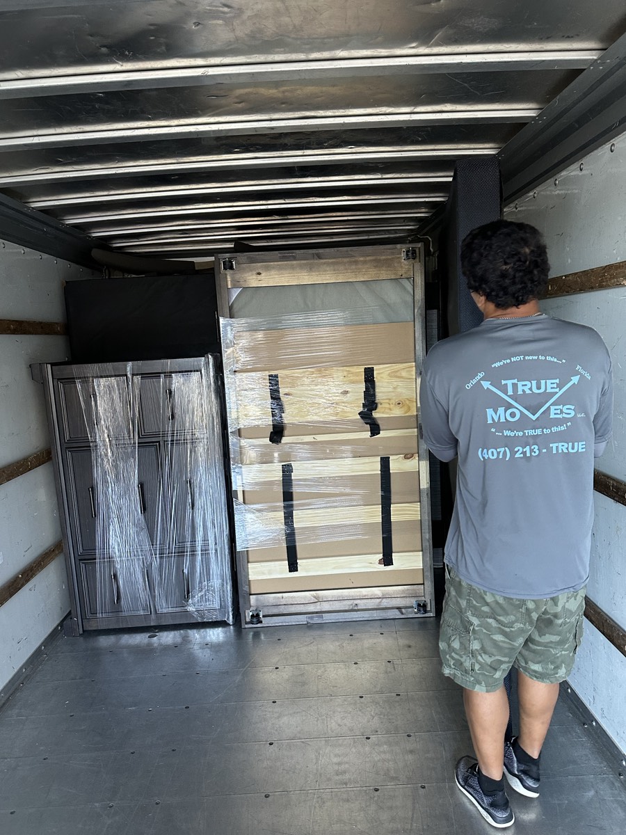 Mover loading a shrink-wrapped dresser into the truck